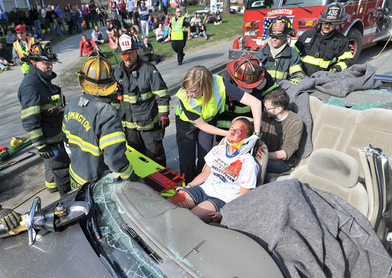 Emergency personnel from Farmington Fire Department and NorthStar Ambulance treat Meghan Plant, 18, in the passenger seat as Renee Clermont, 18, is covered by a blanket in the driver's seat during a mock drunken driving scene on South Street at the University of Maine in Farmington on Thursday. The drill was organized by UMF, NorthStar Ambulance, Farmington Fire Department and Police Departments to illustrate the devastating consequences of drunken driving.