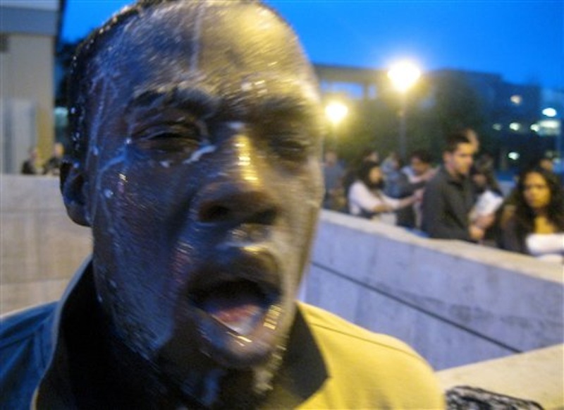 Nnaemeka Alozie, campaign manager for David Steinman, reacts with milk on his face after being sprayed with pepper spray during a protest on Tuesday, April 3, 2012, in Santa Monica, Calif. Campus police pepper-sprayed as many as 30 demonstrators after Santa Monica College students angry over a plan to offer high-priced courses tried to push their way into a trustees meeting Tuesday evening, authorities said. (AP Photo/Courtesy David Steinman)