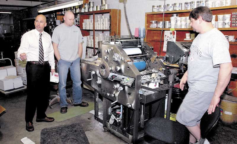 CLOSING: Jim Mitchell, left, co- owner of Atkins Printing Service in Waterville, speaks about the company as employees Randy Lovely, center, and Howard Dyer operate a press. The company is closing this month after 102 years in business.