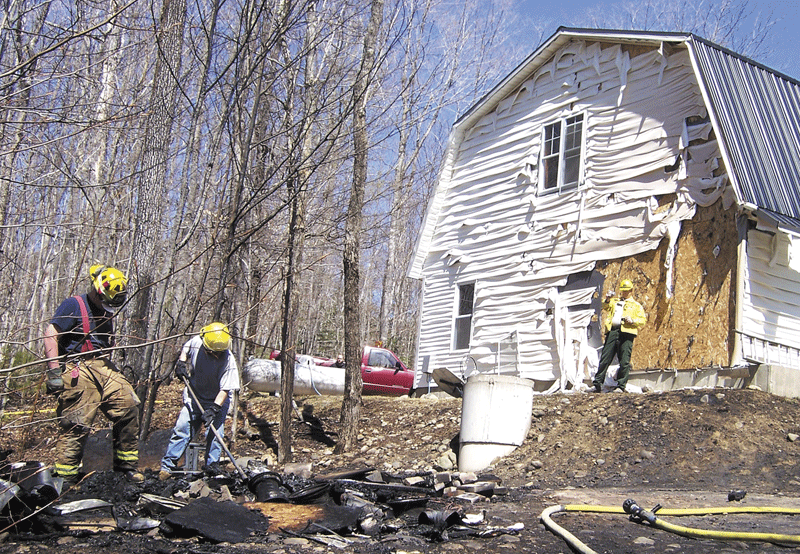 ASH FIRE: Forest Ranger Mark Rousseau watches as firefighters clean up the charred remains of a shed, which was set ablaze Wednesday afternoon by a fire that started in a pile of wood-burning stove ashes. The intense heat melted the vinyl siding on the garage and the 1353 Reeds Mill Road home of Mark and Shelley Keene.