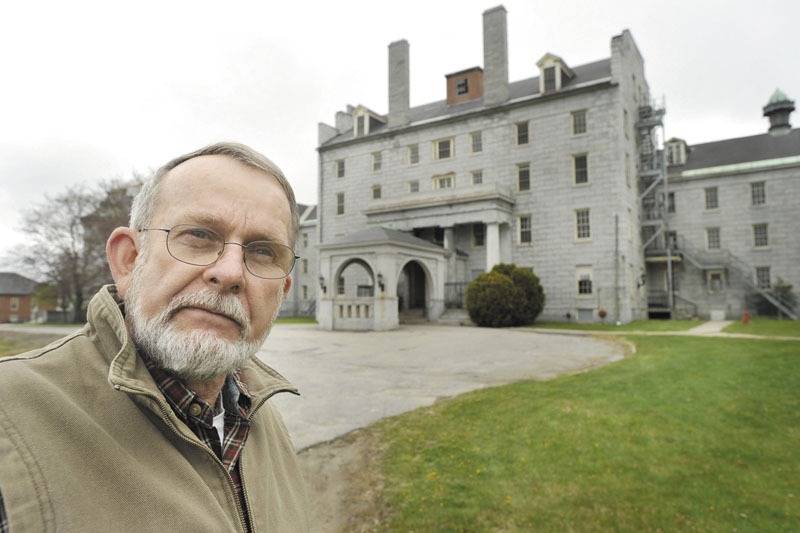 Peter Driscoll, executive director of Amistad, stands in front of the former AMHI building, which now stands empty in Augusta. A Portland-based nonprofit group that serves the mentally ill, Amistad has launched a fundraising effort to build a permanent memorial to those who died at AMHI but whose burial sites are unknown.