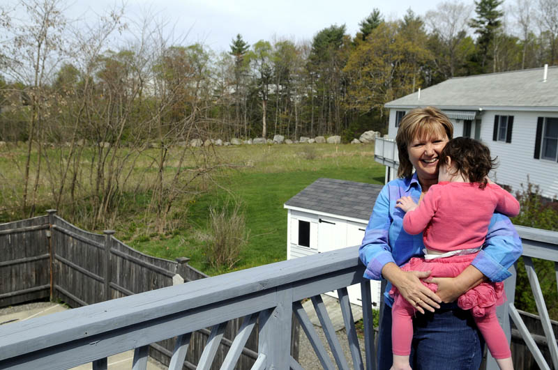 Jean Goding holds her granddaughter, Julia Luszczki, 2, on the deck of Goding's Augusta home Sunday. The proposed site for a new Augusta Spiritualist Church is behind her house, and oding and several other neighbors object to the planned location.