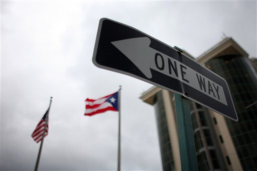 In this May 4, 2012 photo, the flags of Puerto Rico and the U.S. wave behind an English one-way traffic sign in Guaynabo, Puerto Rico, one of only a few places in Puerto Rico with street signs in English. Puerto Rico's Governor Luis Fortuno is trying to do what more than a century of American citizenship has failed to accomplish: teach Puerto Ricans to speak English as well as they do Spanish. (AP Photo/Ricardo Arduengo)