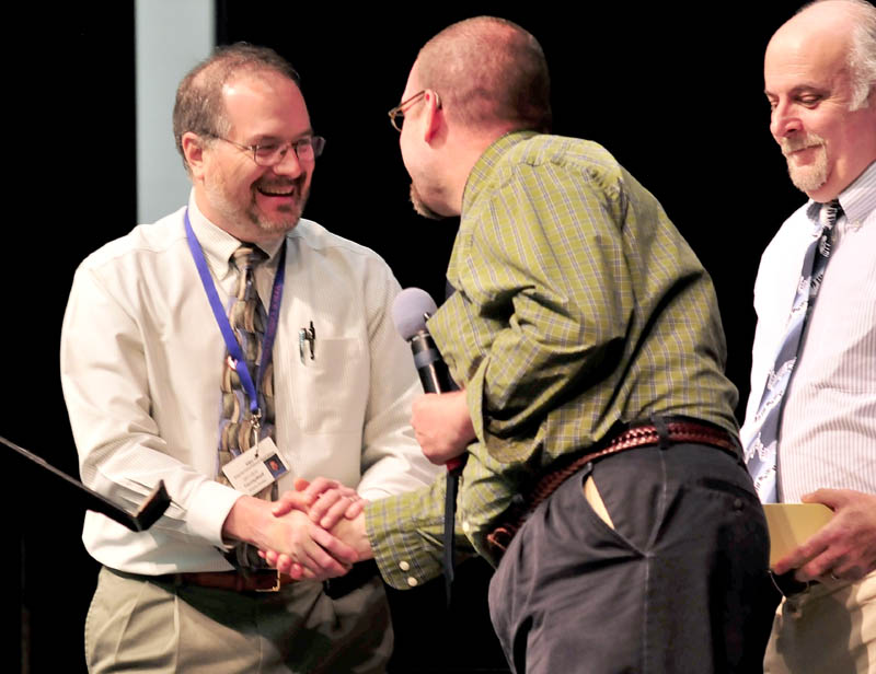 WELL DONE: Messalonskee High School music teacher Andy Forster, left, is congratulated by Mount Blue teacher Steve Muise after it was announced during a school assembly on Tuesday that Forster was named Maine Music Teacher of the Year. At right is Messalonskee teacher Kevin Rhein.
