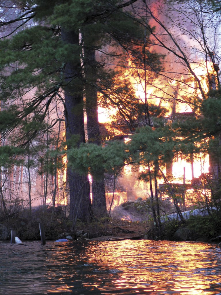 Smoke rises from a house fire on an island in Togus Pond on Friday. A 15-year-old boy has been charged with setting the fire and burglarizing other homes on Coon Island.