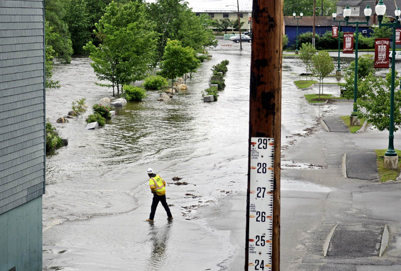 A state Department of Transportation worker inspects flooding Cobbossee Stream in the arcade lot between Gardiner between Bridge Street and Maine Avenue. State crews closed bridges on both roads and city officials removed all the vehicles in the arcade lot ahead of flooding.