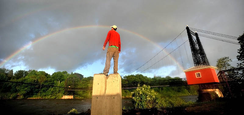 Staff photo by Michael G. Seamans Jesse Hamilton, of Waterville, watches a double rainbow form over the Two-Cent Bridge on the Kennebec River from the Waterville side on Tuesday.