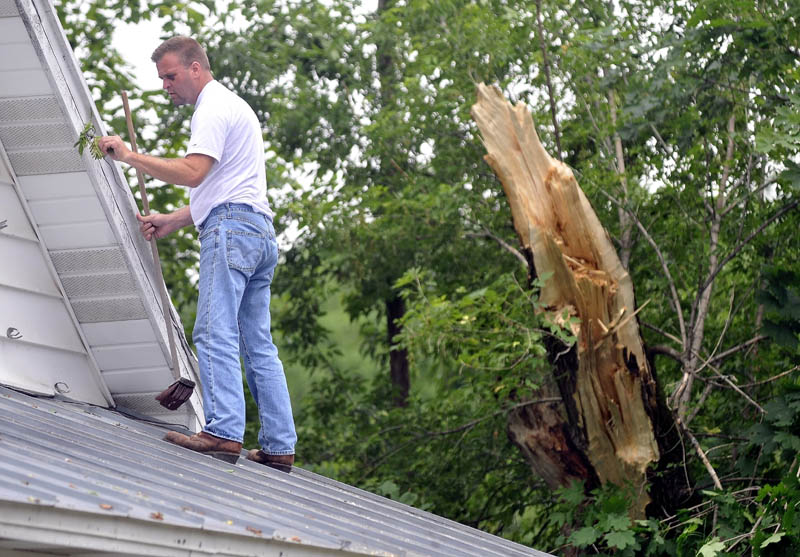 Staff Photo by Michael G. Seamans Dave Cannon Jr. cleans debris from his mother-in-law's home on Drummond Avenue in Waterville on Saturday. Thebroken tree in the background was blown down onto the house during Friday's storm.