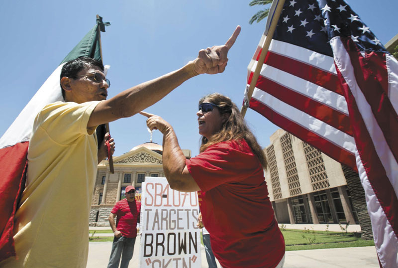 Andy Hernandez, carrying a Mexican flag, and Allison Culver, carrying an American flag argue Monday about SB1070 outside the State Capitol Building in Phoenix. While finding much of the Arizona law unconstitutional, the U.S. Supreme Court said Monday that one part would stand -- the portion requiring police to check the status of someone they suspect is not in the United States legally. SB1070
