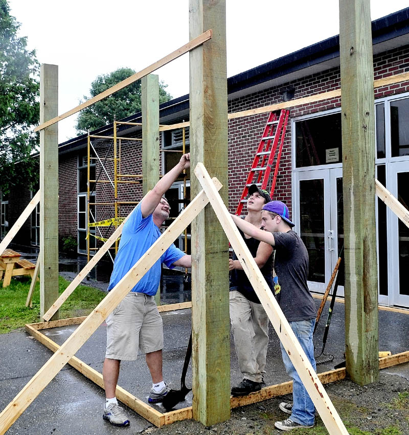 UP AND AWAY: Instructor Jim Easler, left, helps Carrabec High School students Kenneth White, center, and Anthony Toneatti build a portico entry structure in front of the North Anson school on Tuesday.