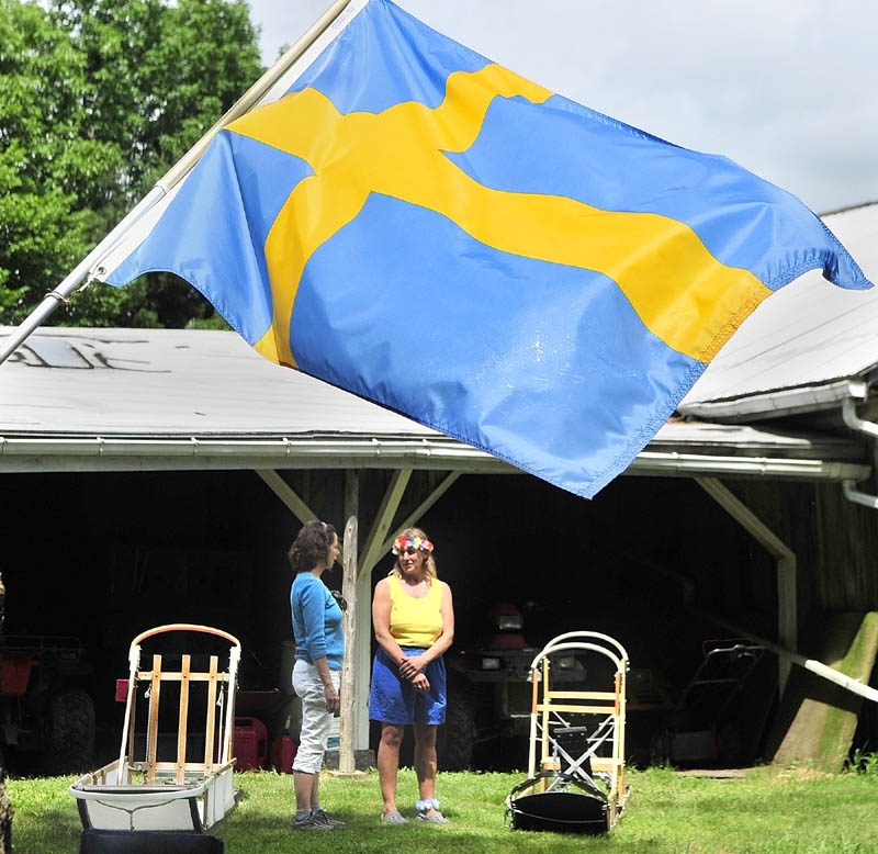A Swedish flag floats in the breeze above Paula Sutton, of Warren, left, and Heywood Kennels co-owner Lindy Howe as they chat beside dog sleds on Saturday in Augusta.