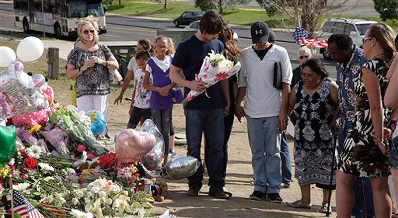 Actor Christian Bale, holding flowers at center, joins hands and prays with visitors to a memorial to the victims of Friday's mass shooting, Tuesday, July 24, 2012, in Aurora, Colo. Twelve people were killed when a gunman opened fire during a late-night showing of the movie "The Dark Knight Rises," which stars Bale as Batman. (AP Photo/Ted S. Warren)