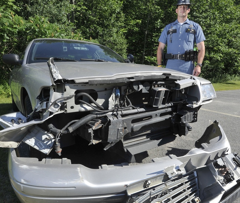 Maine State Police trooper Douglas Cropper stands beside his police car that was damaged while stopping a wrong way driver on I-295.