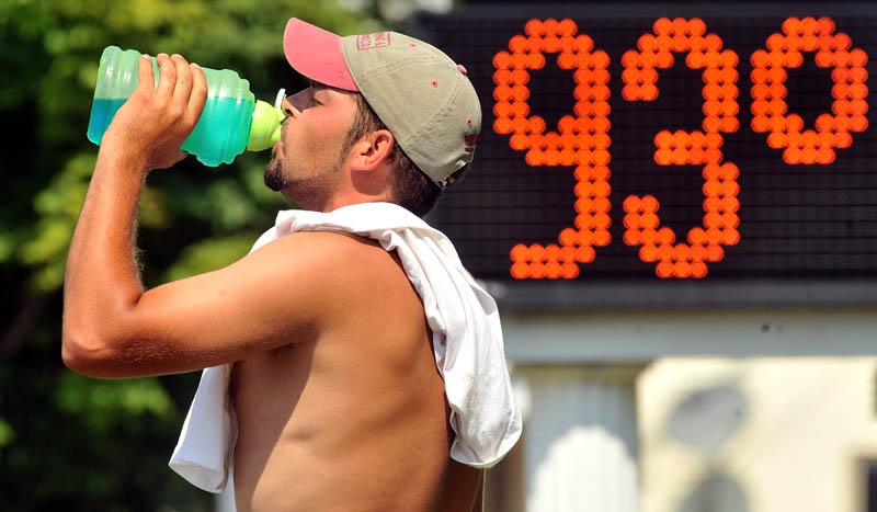 Josh Taylor, a worker with Stevens Siding and Window, hydrates Friday at a job sight next to the Skowhegan Savings Bank on Main Street in Fairfield, where a sign indicates the hot temperature.