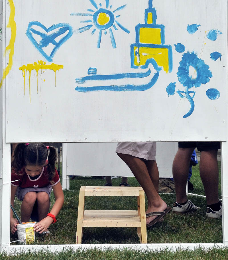 Addison Lopes, 6, grabs paint and a brush as she adds her artistic impression to the wall provided by Common Street Arts in Castonguay Square during the Waterville Intown Arts Festival on Main Street on Saturday.