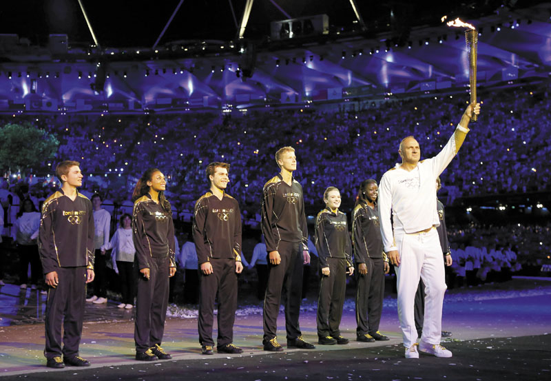 Olympic gold medalist Sir Steve Redgrave, right, holds the Olympic torch after entering the stadium during the opening ceremony at the 2012 Summer Olympics on Saturday in London. Redgrave handed the flame off to the young athletes behind him, who in turn lit the Olympic cauldron.