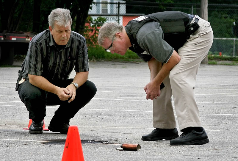 Staff photo by Ben McCanna Winslow Police Chief Jeffrey Fenlason, left, and State Fire Marshal supervisor Ken Grimes examine the remains of an exploded device in the Winslow Junior High Schooll parking lot Thursday. It was the third device exploded in Winslow in the last three days.