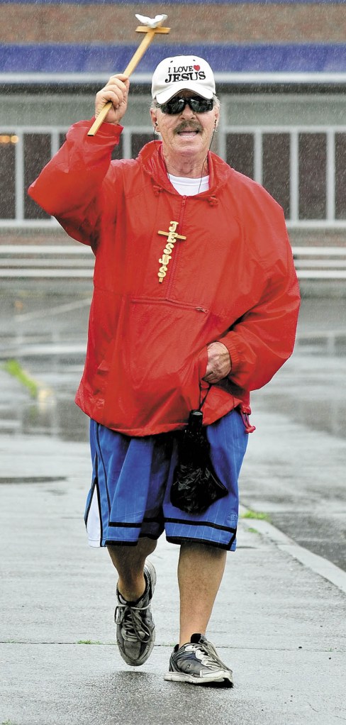 BLESSINGS: John Lewis, seen walking the streets of Waterville with a cross last month, died Tuesday. Lewis said in June that he has been blessing people and everything for 40 years. "I bless things wherever the Lord sends me," he said. As for his opinion on the rain, Lewis said, "It doesn't matter — be happy."