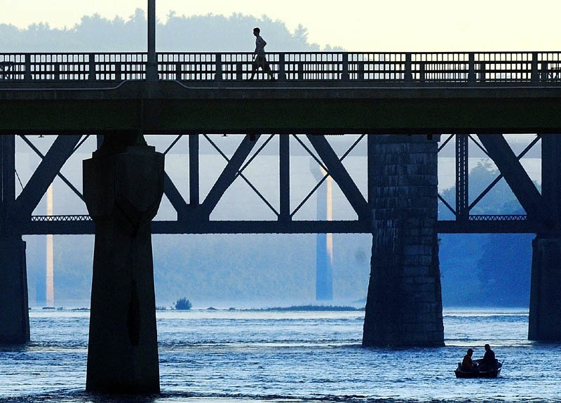 A walker crosses the Calumet Bridge at Old Fort Western over a duo of fishermen in a boat on the Kennebec River on Saturday morning in downtown Augusta. There were only two boats out as the sun was rising over the hills and the tide was going out.