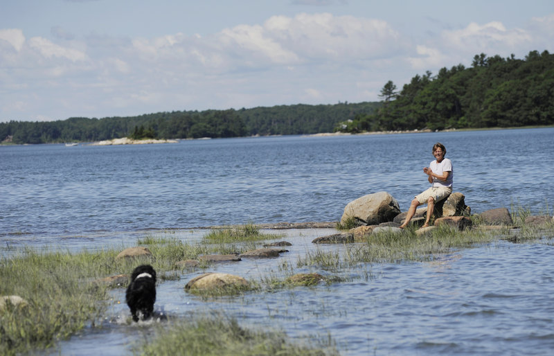 Linda Fraser-Campbell calls for her dog, Lady, to join her on some rocks along the shore at Middle Bay Cove at the end of a trail at Skolfield Shores Preserve in Harpswell. Fraser-Campbell, who lives near the property, says she hikes the trails twice a day.