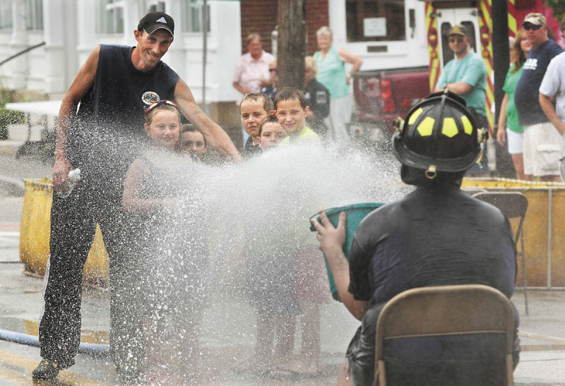 Richmond Firefighter Jason Gilpatric, left, helps some area youngsters spray a hose at firefighter Michael Baglieri, right, as he tries to a bucket at the Fireman's Muster event on Saturday at Richmond Days.
