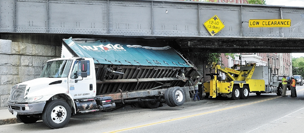Staff photo by Joe Phelan KDT Towing workers remove a box truck stuck under the railroad trestle Thursday morning on Water Street in downtown Augusta.
