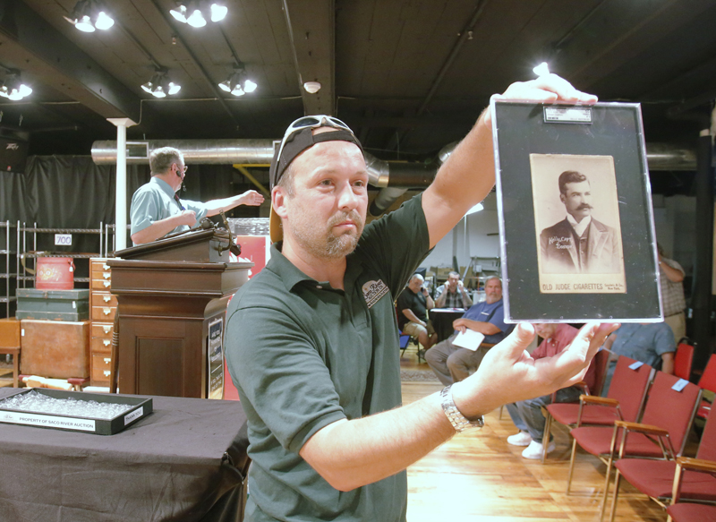 Don Hartford of Saco River Auctions holds up a baseball card of King Kelly of the 1888 Boston Beaneaters during an auction at tbe auction house in Biddeford on Wednesday evening. The card, which is only one of four known to exist in the world, sold for $62,000. Auctioneer Floyd Hartford conducts the bidding in the background.