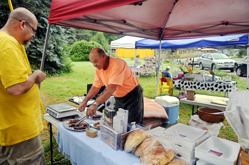 Ian Cundiff, left, samples sausage prepared by vendor Bill Trussell at the Belgrade Village Market across from the Sunset Grille on Sunday morning. Cundiff sells baked items with his wife, Julie, at the market.