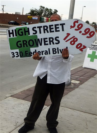A sign-spinner outside a west Denver medical marijuana dispensary advertises low-cost pot as rush hour drivers pass the pot shop on Monday.