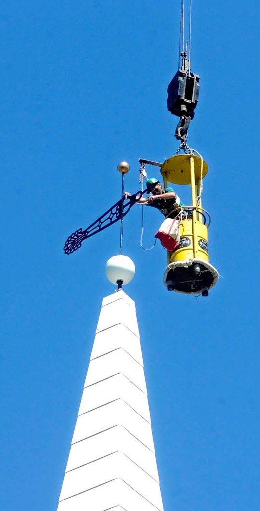 Staff photo by Joe Phelan Working from a bucket hanging from a crane, steeplewright Robert Hanscom put a new weathervane on top of the new steeple he built on Tuesday morning at the corner of Middle and Central Streets in Hallowell.