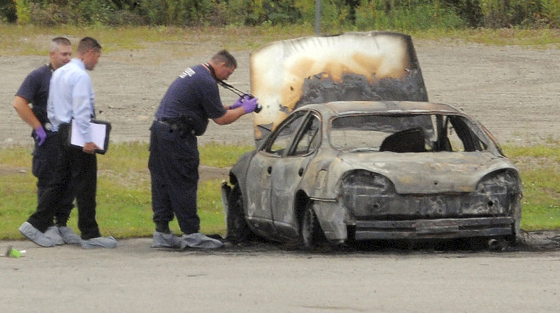 Police investigate the burned vehicle where three bodies were found on Monday in Bangor.