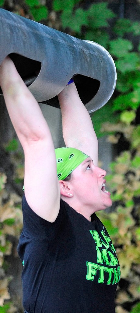 HOIST: Andrea Shorey, of Clinton, strains to lift the bar overhead in the log clean and press event during the Downtown Throwdown strongman contest on Front Street Saturday morning in downtown Augusta.