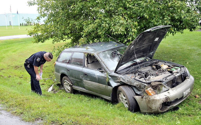 Waterville police Officer Galen Estes inspects Nancy Ross' car after it rolled over during an accident on West River Road in Waterville Wednesday morning.