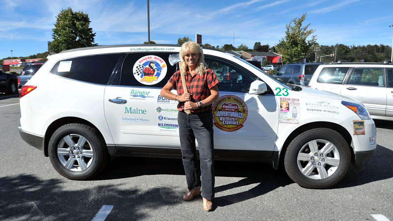 Staff photo by Michael G. Seamans "Timber Tina" Scheer, owner of the Great Maine Lumberjack Show, poses in front of her Fireball Run Adventurerally car at the Bangor Savings Bank on Main Street in Waterville. Scheer and her driving partner depart for Independence, Ohio on Thursday.