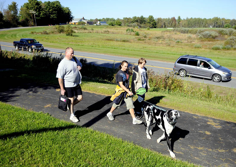 Staff photo by Andy Molloy NEW DIRECTION: Chris, left, and Stacey Shaw walk their son, Robert, 13, home Tuesday from Maranacook Community School in Readfield on the new sidewalk that connects the middle and high schools to the town hall in Readfield along Route 17.