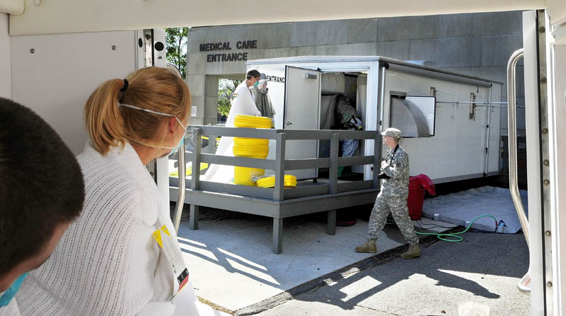 Staff photo by Joe Phelan A Togus VA Medical Center staffer in a suit , center, leads a person playing a victim exposed to anthrax into the decontamination shed as another "victim" watches from inside an ambulance during a full scale joint Mass Casualty exercise on Tuesday at the Togus VA Medical Center. Five students from the Capital Area Technical Center Law Enforcement program went through the decontamination shed as part of the exercise.
