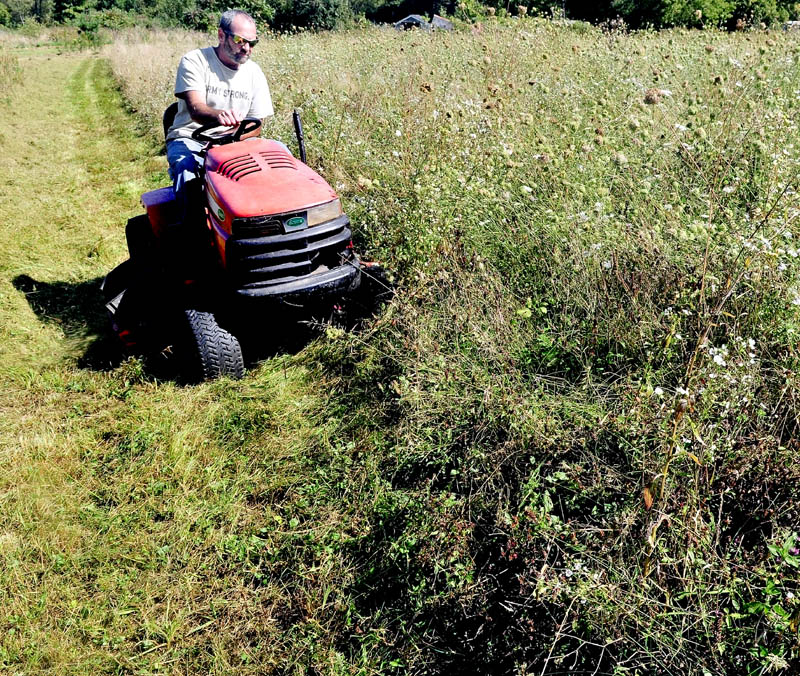 GAS SAVER: Mike Dyer slowly cuts 2-foot high grass at his home in Vassalboro on Monday. "I'm knocking this grass down now because it's getting big," Dyer said. Gas was high this summer so I didn't bother to mow."