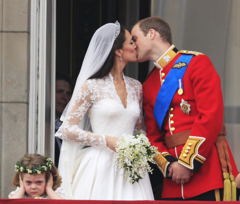 As bridesmaid Grace van Cutsem, left, covers her ears, Britain's Prince William kisses his wife Kate, Duchess of Cambridge, on the balcony of Buckingham Palace after the Royal Wedding in London Friday, April, 29, 2011.