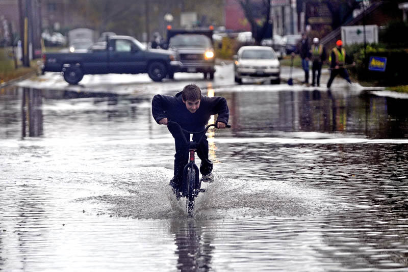 Hunter Desveaux rides his bicycle through flood waters on Front Street after heavy rains fell on Waterville Tuesday.