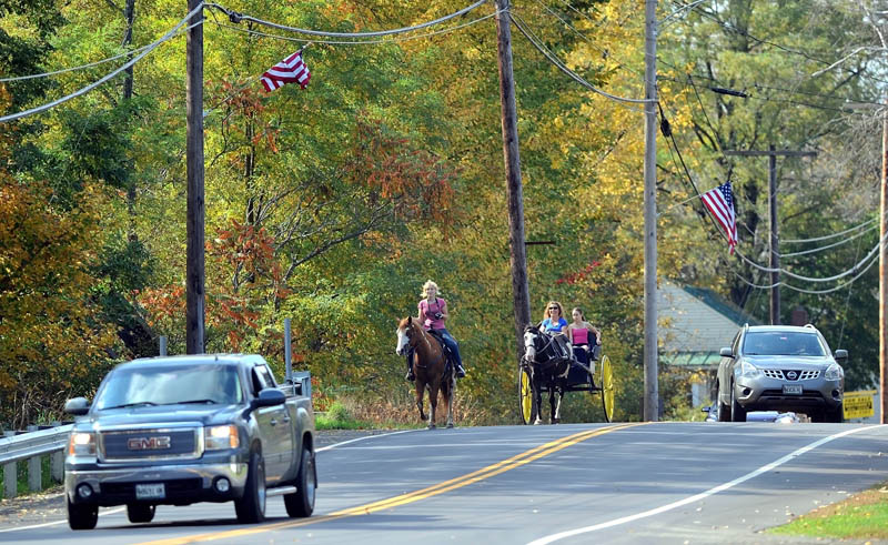 Charlene Bigelow, 18, rides her horse, Cider, as Alice Hadley drives her cart with Emily Fortier, 12, down HWY 16 in North Anson on Friday.