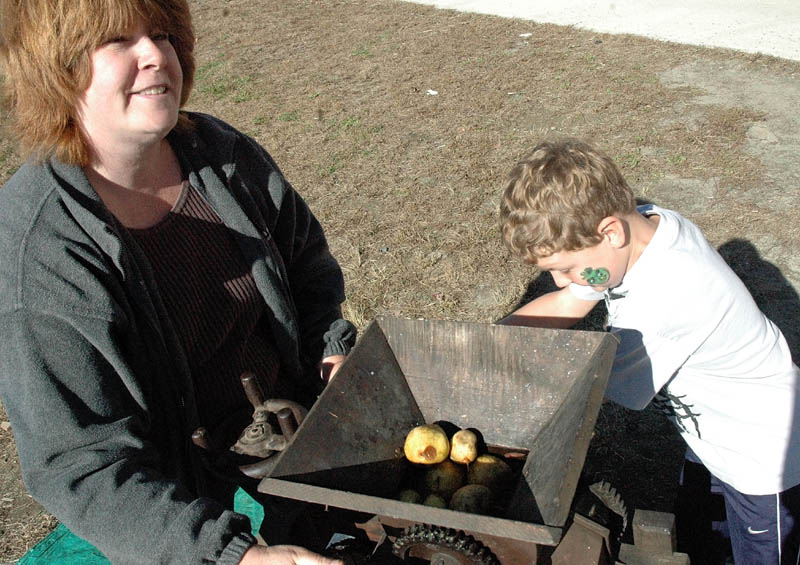 Kim Richards, education technician, and Haden Daigle, 8, make cider with an apple press at the Applefest at the Mill Stream Elementary School in Norridgewock Saturday.
