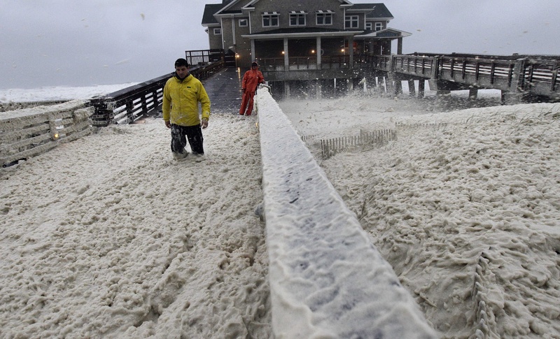 A news crew wades through sea foam blown onto Jeanette's Pier in Nags Head, N.C., on Sunday, as wind and rain from Hurricane Sandy move into the area.