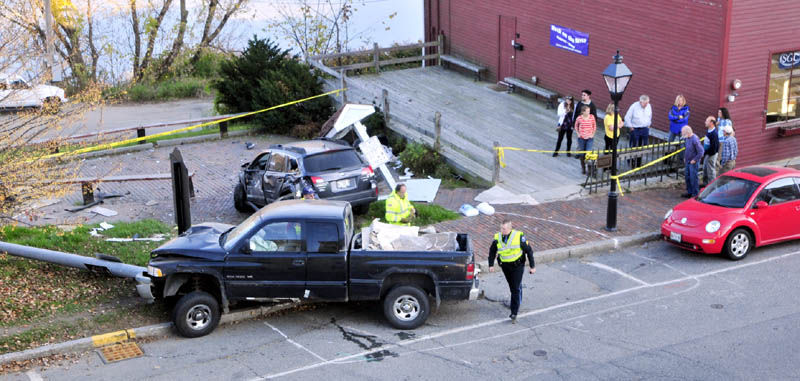 Hallowell police and firefighters clean up at the scene of an accident on this afternoon at the corner of Water and Winthrop Streets in downtown Hallowell. The pickup truck, front left, was traveling down hill on Winthrop Street when it struck a parked vehicle, top, which was then slammed into a sign board. The truck also knocked over a light post before stopping in the sidewalk. Two people in the truck were injured.