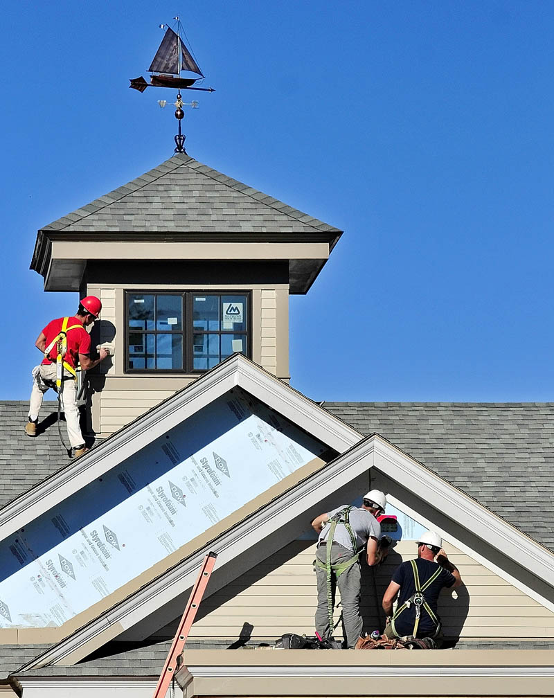 Workers paint trim and install siding on Thursday afternoon at the new Kennebec Savings Bank branch being built at the corner of Northern and Maine avenues in Farmingdale. The new building is designed to resemble the 1826 mansion that was removed earlier this year.