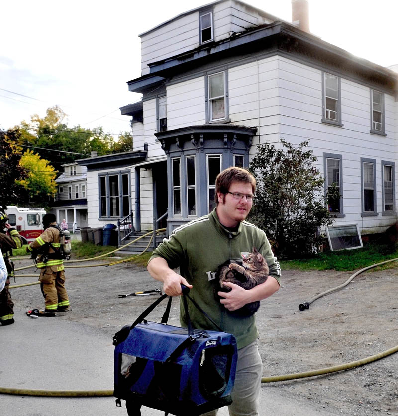 SAVED: Bill Laymon carries his cats Malcolm, in arms and Lenore, in bag, that firefighters rescued from the apartment, background, that sustained serious fire damage on Western Avenue in Waterville on Tuesday.
