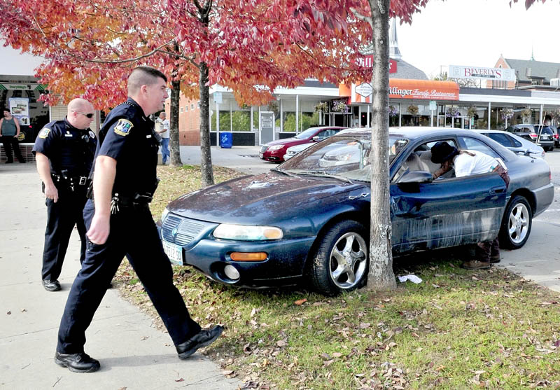 Waterville police officers Dennis Picard, left, and Galen Estes watch as a woman retrieves items from a vehicle that stopped against a tree in The Concourse on Tuesday pinning the woman driver's leg in the open door.