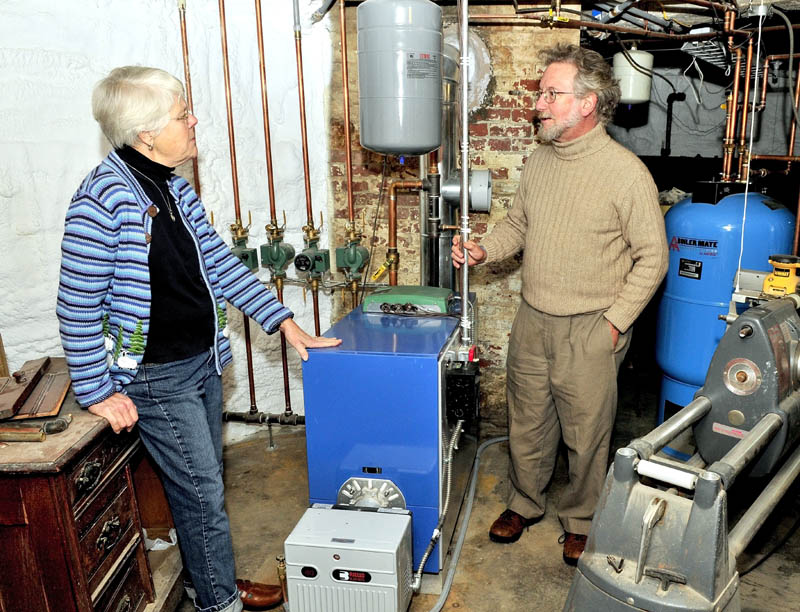 The Revs. Alice and David Anderman speak about the weatherization program they participated in beside a new energy-efficient furnace, hot water tank and foam insulation-covered walls in the basement of their home in Waterville.