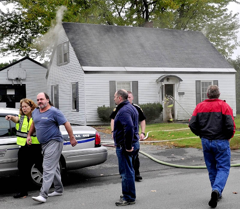 Tenant Jeff Macklin is escorted away from his burning home by Fairfield police officer Karen O'Donnell as firefighters enter the building on Military Avenue on Monday. Officer Jacob Pierce, background, entered the home and got Macklin out of the house.
