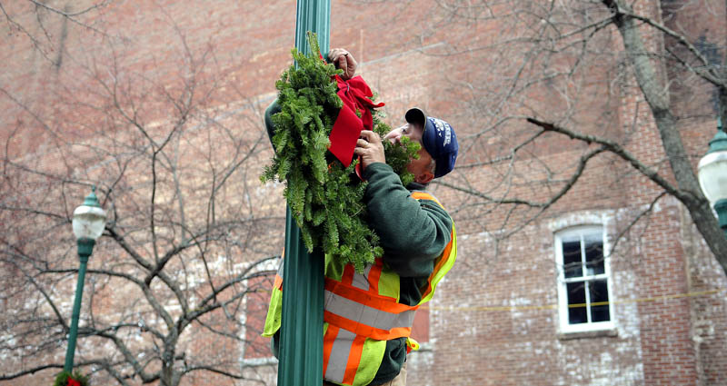 Gardiner Buildings and Grounds Supervisor Pat Chadwick hangs a wreath Wednesday on Water Street. Gardiner crews were preparing the downtown for the annual Christmas tree lighting, scheduled for Saturday at 6 p.m.