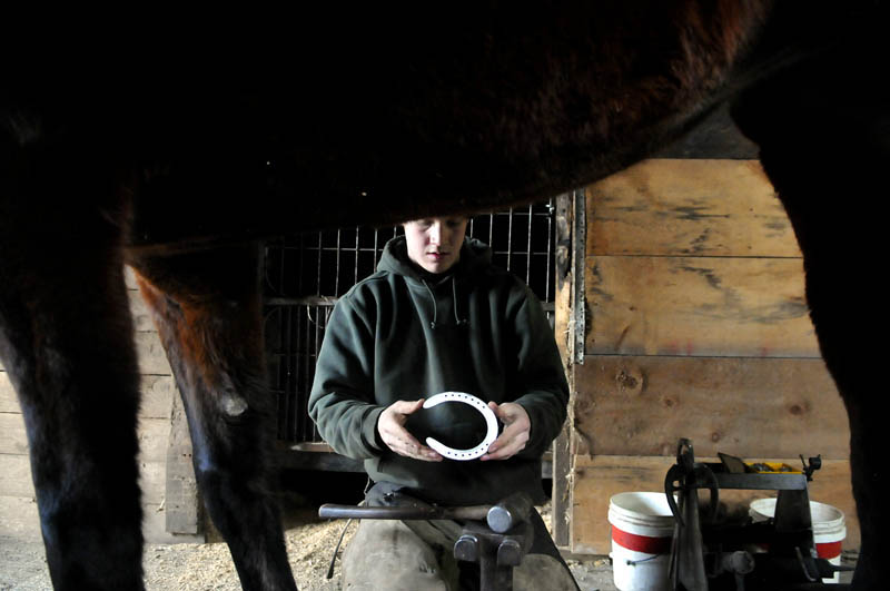 Farrier Scott Hickey examines a horseshoe he pounded Tuesday for a pacer, in the stalls at the Windsor Fairgrounds. Hickey, 22, of West Gardiner, said that the metal arches have to be level before being nailed to the hoof.